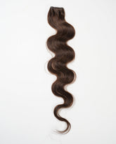 A single bundle of long, dark brown, wavy virgin hair extension is displayed on a white background.