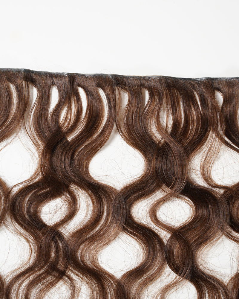 Wavy brown hair extensions are laid flat against a white background, highlighting the natural texture and loose waves of each strand.