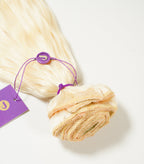 Platinum blonde hair extensions bundled with a purple tag and elastic band, arranged neatly on a white surface.