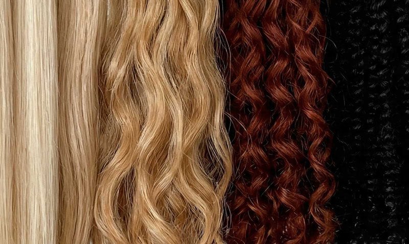 Four sections of hair in different colors and textures: straight platinum blonde, wavy light blonde, curly auburn, and tightly coiled black hair, all shown side by side.