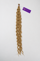 A bundle of long, curly blonde hair extensions with a purple brand tag, displayed against a plain white background.