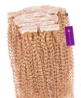 Kinky Curly Classic Clip In Hair Extensions by Perfect Locks in honey blonde curls with a purple tag, shown on a white background.#color_honey-blonde-(27)