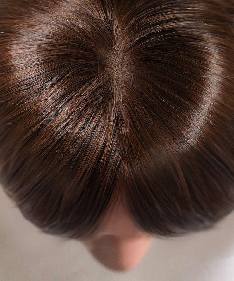 Close-up of a person's head with healthy, shiny medium brown hair parted off-center and a seamlessly blended hair crown topper.
