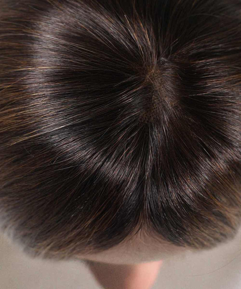Close-up view of a person's head with dark, shiny hair in warm mocha lowlights, parted at the center to reveal the scalp.