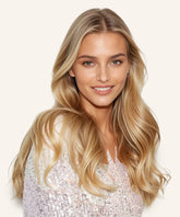 A woman with long, straight Honey Blonde hair wears the Straight Lace Front Wig by Perfect Locks, smiling in a sparkly light top against a plain background.#color_honey-blonde-(27)