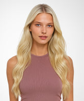 A young woman with long, Platinum Blonde hair styled in a Straight U-Part Wig wears a sleeveless mauve top, calmly gazing at the camera.#color_platinum-blonde-(613)