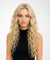 A woman wears the Perfect Locks Wavy U-Part Wig in Platinum Blonde, blue eyes, black ribbed top, white background, neutral expression.#color_platinum-blonde-(613)