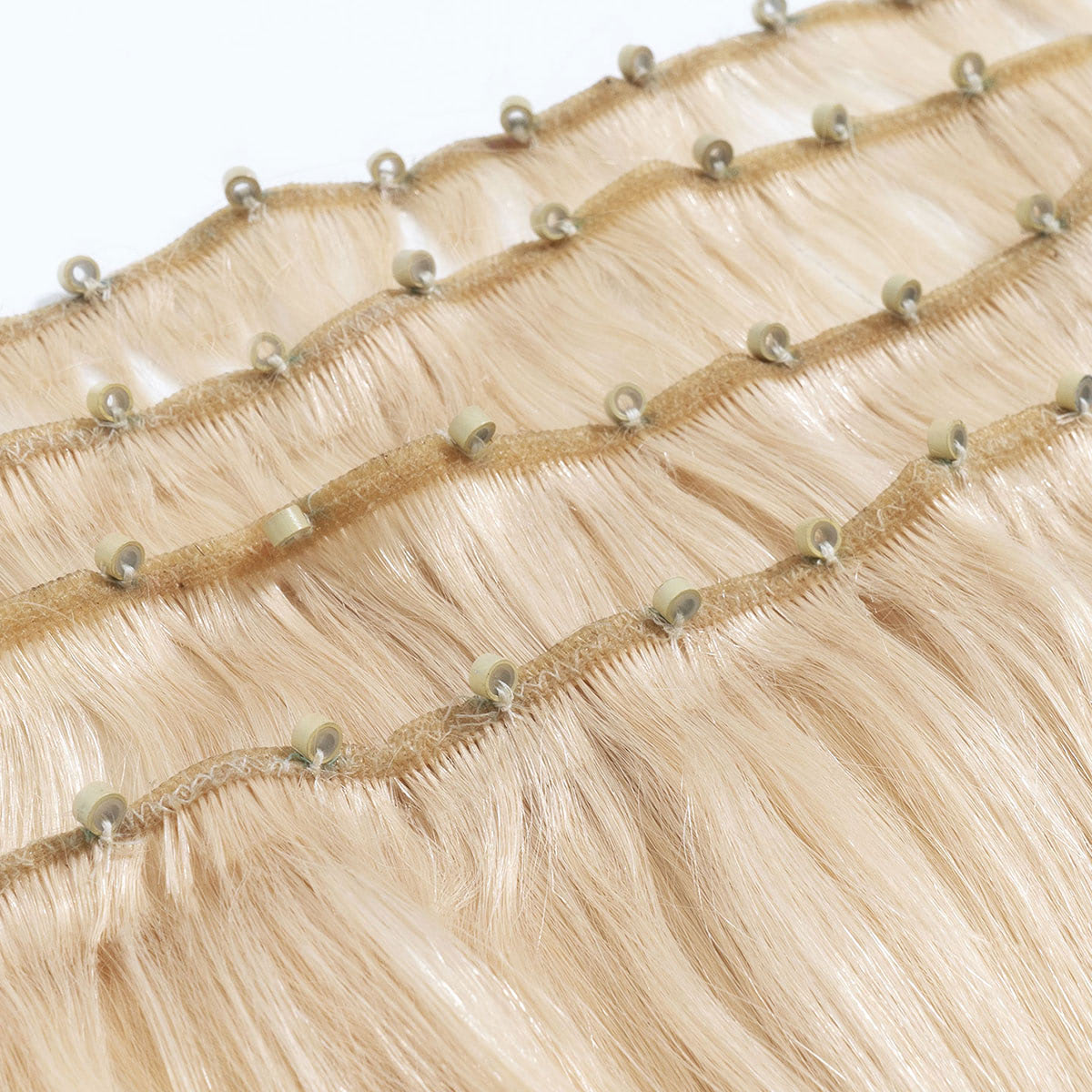 Close-up of several rows of straight, light blonde hair extensions with small beige beads along the seam for seamless installation.