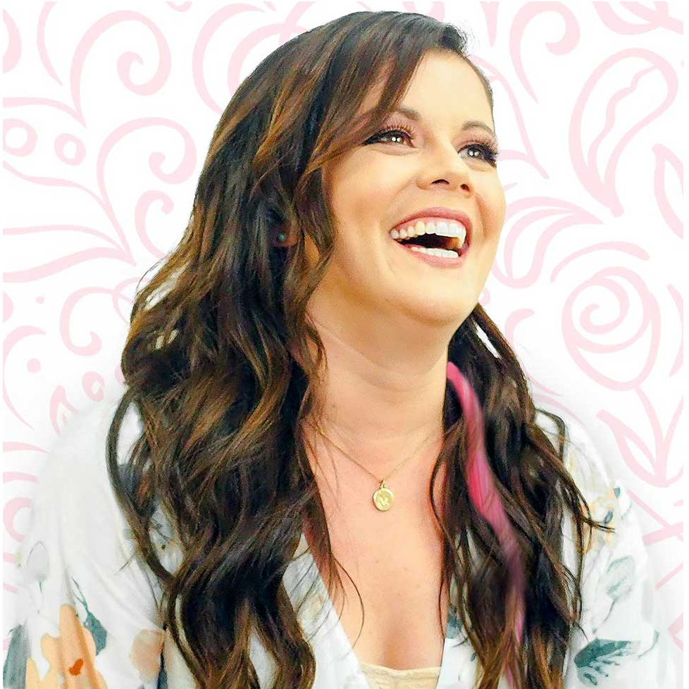 Woman with long wavy hair and a floral outfit against a pink patterned background