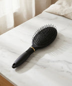 Matte black hair extension loop brush with looped bristles and gold trim resting on a white marble countertop.