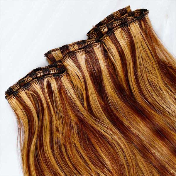 Close-up of honey brown and blonde hand tied weft hair extensions showing the stitched tracks and smooth, glossy strands