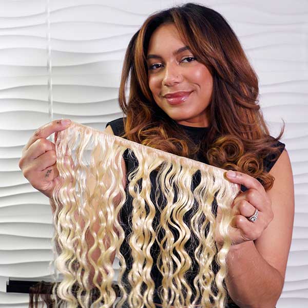 Woman holding a bundle of blonde hair extensions against a white background