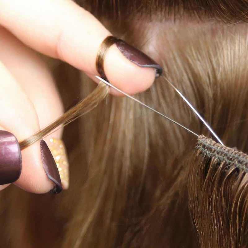 Step 2: Gather a section of hair. Thread the first bead on the edge of the beaded weft onto natural hair ...