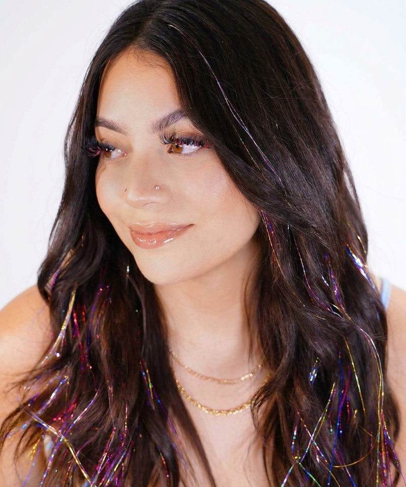 Shimmering multi-colored hair tinsel strands styled throughout long, wavy dark brown hair.