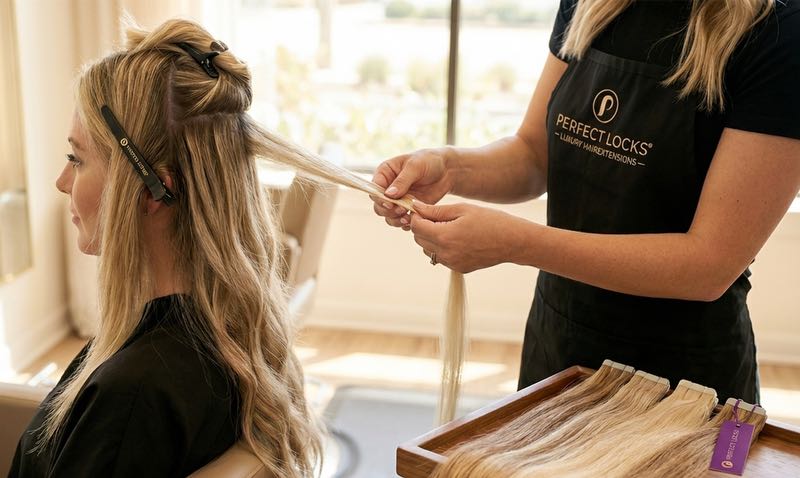 Person getting tape in hair extensions installed by a professional in a salon setting.