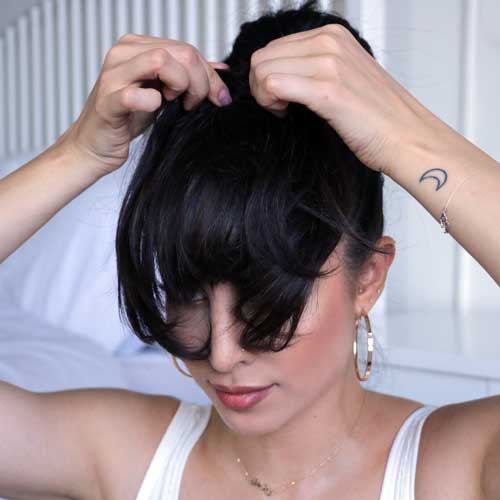 beautiful woman trying on clip in bang hair extensions in natural black hair color