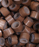 Close-up of Perfect Locks Fusion Micro Ring Beads in dark brown, small hollow cylindrical beads, stacked and scattered for hair extensions.#color_dark-brown-(4)