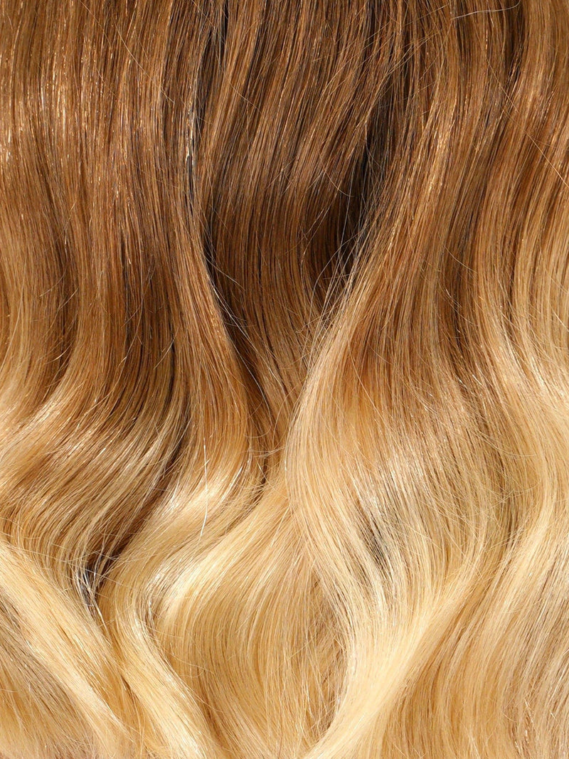 Wavy hair with a brown to blonde ombre gradient shines smoothly, featuring a seamless transition from darker roots to lighter ends.