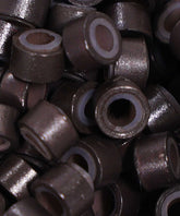 A close-up of Perfect Locks Fusion Micro Ring Beads in natural black, featuring small, cylindrical metal parts with a hollow center and textured surface—ideal for securing Remy hair extensions.#color_natural-black-(1B)