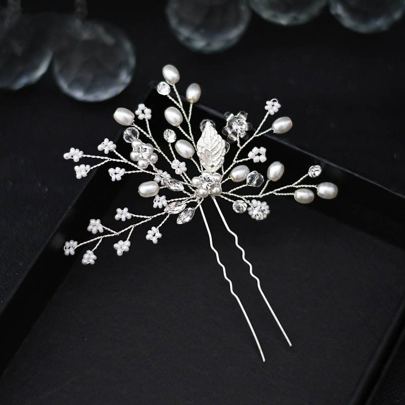 A delicate silver hairpin adorned with small white pearls, clear crystals, and intricate floral wirework sparkles elegantly on a black background.