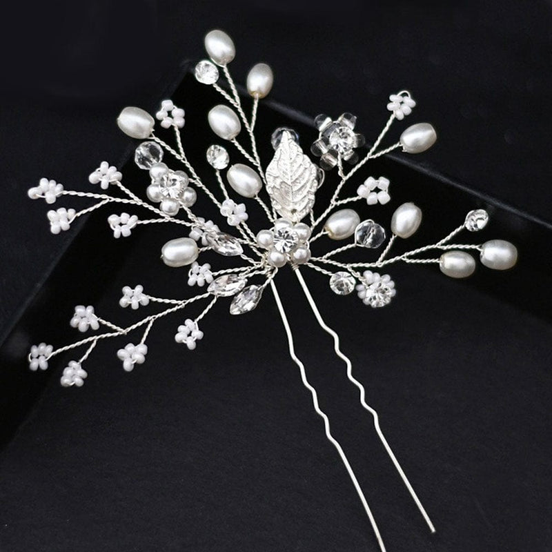 A delicate silver hairpin adorned with small white pearls, shimmering crystal beads, and silver leaves in a floral branch-like design stands out against a black background.
