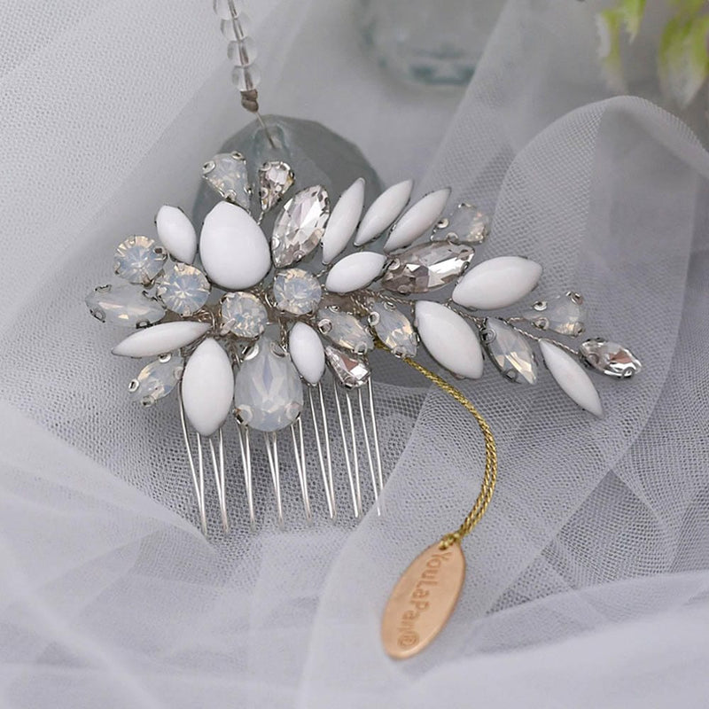 A decorative hair comb adorned with white and clear gemstones in a floral pattern, gold chain, and oval tag on sheer white fabric.