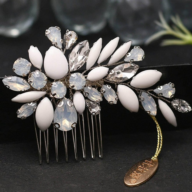A decorative hair comb with white and clear crystal gemstones in a floral pattern, gold tag attached, shimmering on a dark surface.