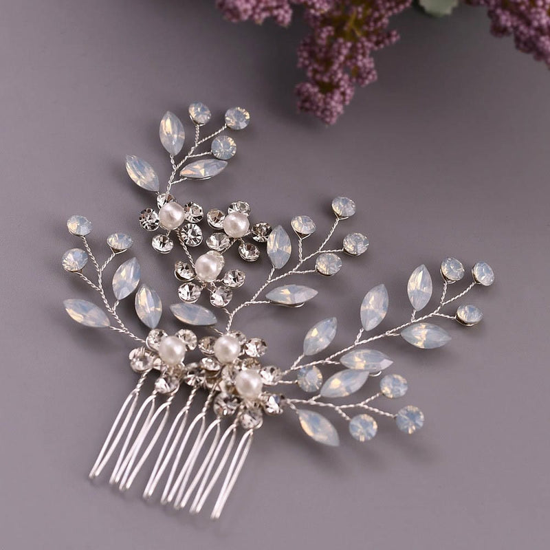 A decorative silver hair comb with pearl and crystal embellishments in a floral leaf pattern rests on gray, purple flowers behind.