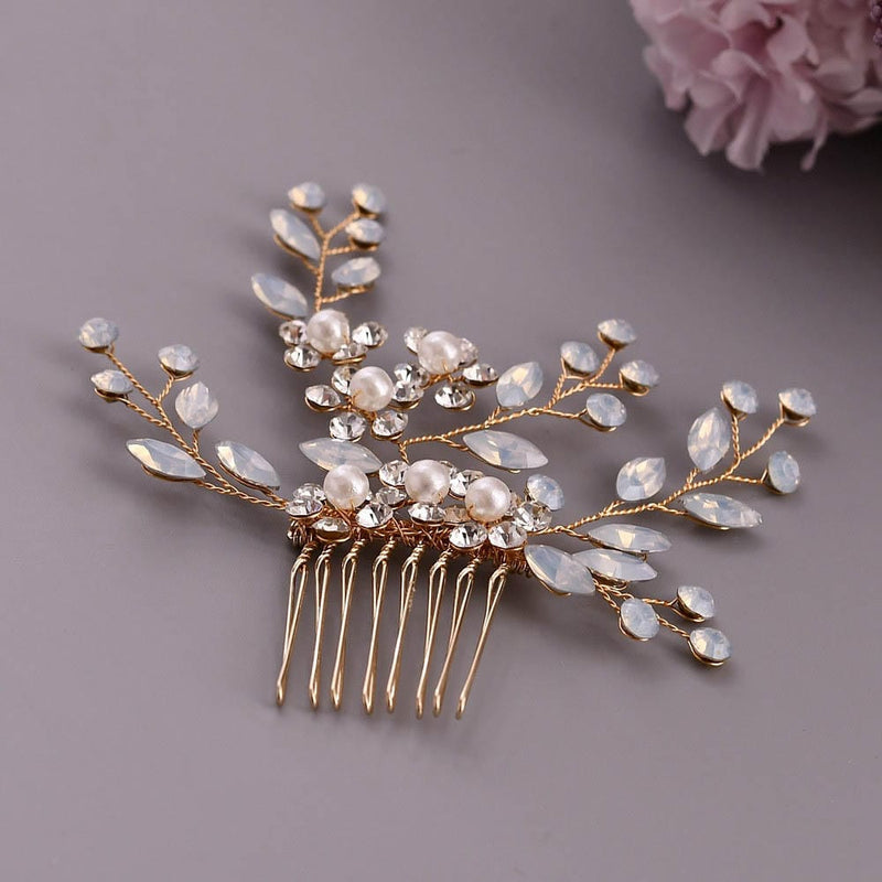 A decorative gold hair comb with pearl and crystal accents in a leafy branch design; a soft pink flower blooms in the background.