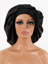 A mannequin with a medium skin tone wears a shiny black satin bonnet with a bow on the front, displayed against a white background.