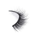 A single strip of black false eyelashes with thick, long, wispy fibers and a natural curl enhances the lash line on white background.