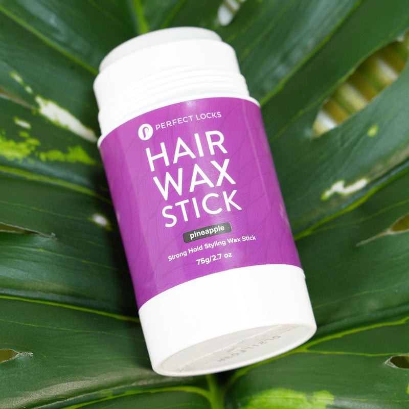 A purple and white container labeled Perfect Locks Hair Wax Stick, featuring pineapple and Strong Hold Styling Wax Stick, 75g/2.7oz, rests on a large green leaf background.