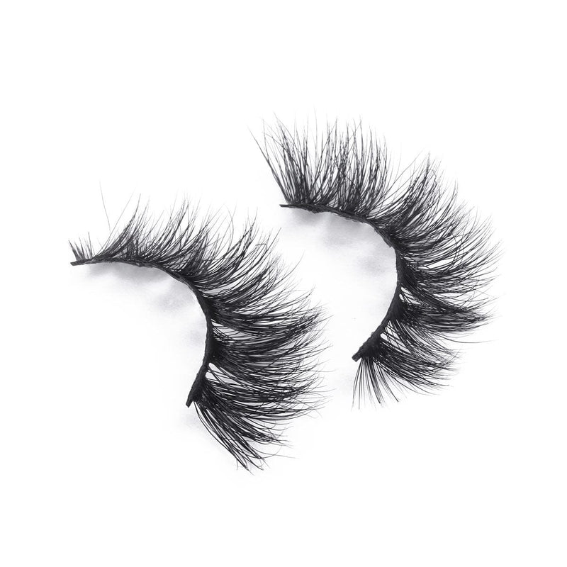 A pair of thick, wispy, black false eyelashes with curled ends adds bold drama against a white background.