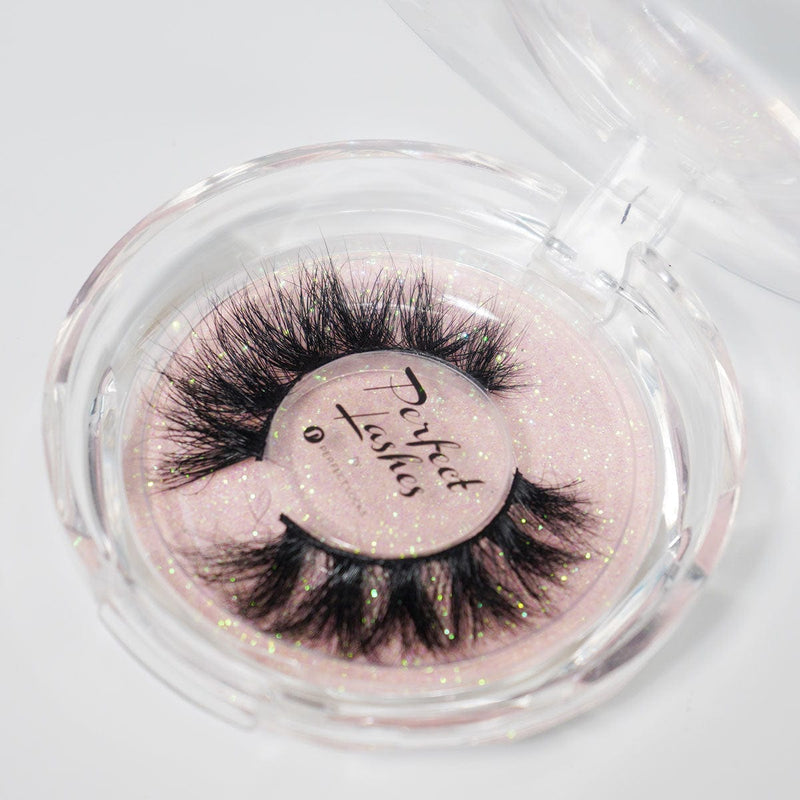 Dramatic, thick false eyelashes in a round, clear plastic case with a sparkly pink base labeled Perfect Lashes as an eye-catching accessory.