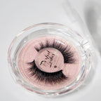 A pair of dramatic, fluffy false eyelashes labeled “Perfect Lashes” in a clear round case with a pink glittery background.