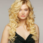 A confident woman with long, wavy blonde hair and fair skin wears a sleeveless black top, posing against a neutral backdrop.